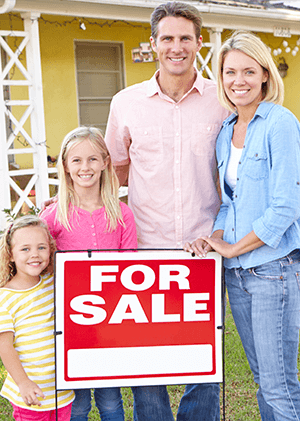 family in front of their house with a for sale sig